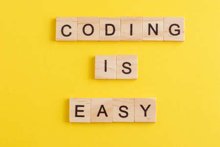 Word Coding is easy made from wooden letters on yellow background. Concept of learning programming...