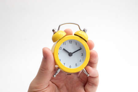 Hand holding yellow alarm clock on light background. Time concept. Keep your time.