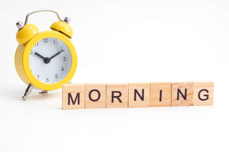 Yellow alarm clock with bell and morning text from wooden cubes.