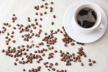 Sprinkled roasted coffee beans and a white cup of coffee. Morning coffee for breakfastの写真素材