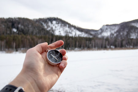 Male hand with compass in winter mountains. Black magnetic compass on traveler's hand for navigation guide. Traveling and exploring concept.の写真素材