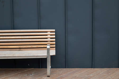 Empty wooden bench against a black wall.の写真素材