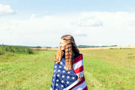 Happy young girl with curly hair wrapping in american flag on field.の写真素材