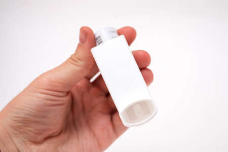 Hand holding asthma inhaler on white background.