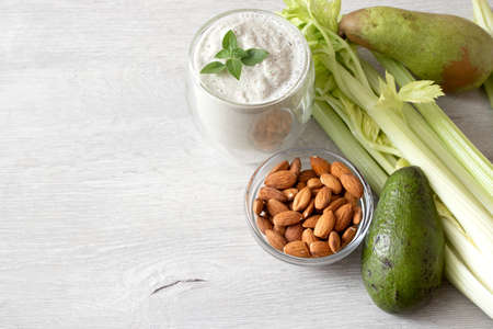 Mix of fresh green vegetables: avocado, celery, almonds, pear and green smoothie on table with space...