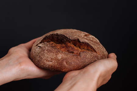 A loaf of rye bread in his hands on a black background.