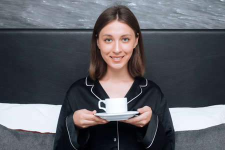 Young woman in bed with a cup of coffee.