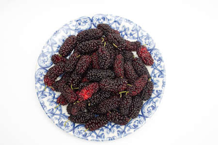 Lots of ripe juicy mulberries on a plate top view