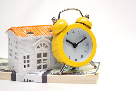 Bundle of dollars and yellow Alarm clock and home model on white background. Time for a loan or mortgageの写真素材