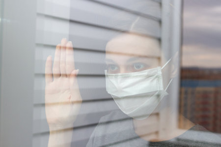 Scared and panic young woman in medical mask behind a glass doorの写真素材