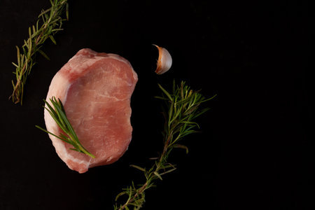 raw piece for steak of meat with rosemary branches on a black backgroundの写真素材