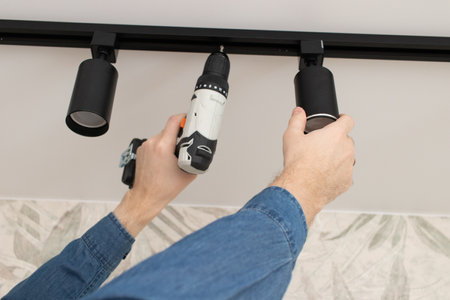 A man repairs a ceiling spot track LED light in the house.の写真素材