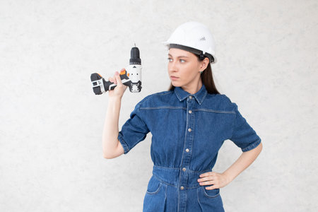 A young female construction worker in a white helmet and with a screwdriver shows a thumbs upの写真素材