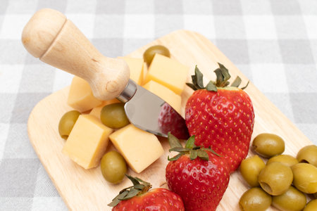 A plate of assorted cheese, strawberries, green olives and a cheese knife.の写真素材