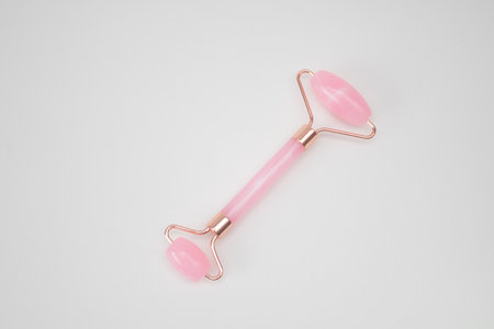 Roller Facial Massager pink quartz stone on white background.の写真素材