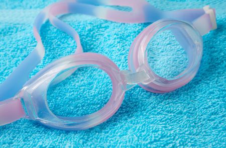 Pink swimming glasses on a blue towelの写真素材