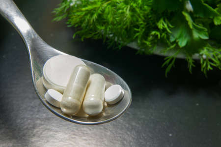 Pills in a spoon versus greens on plate, with black gradient background. Pills vs greens symbolizing choice between healthy diet and frequent drug use.の写真素材