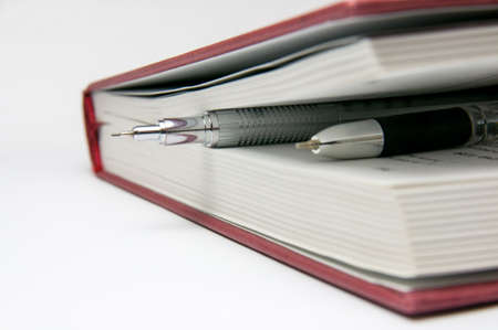Silvery mechanical pencil and pen between the pages of a closed red book.の写真素材