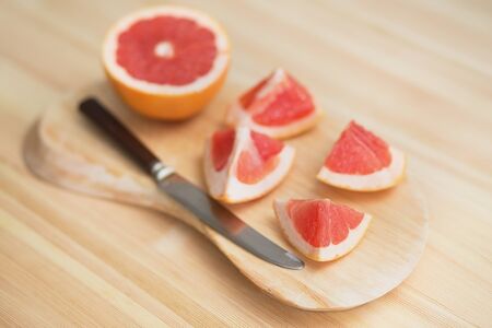 slices of grapefruit on a wooden board with knife
