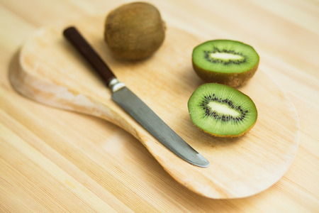 Juicy kiwi fruit with knife on cutting board on wooden background