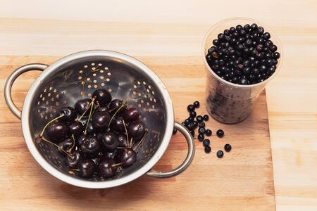 bowl of cherry and cup blueberries on the wooden boardの写真素材