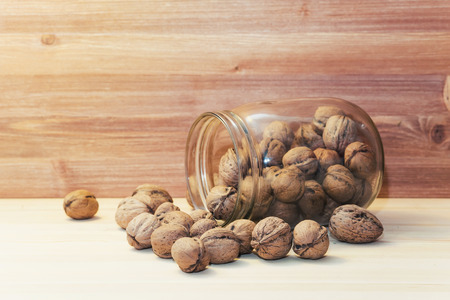 Fresh walnuts in shells falling out of glass jar on wood table backgroundの写真素材