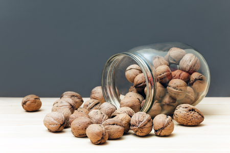 Fresh walnuts in shells falling out of glass jar on wood table background