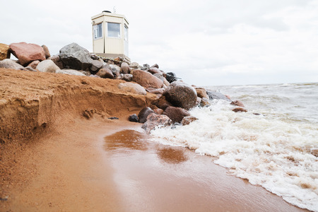 Lighthouse on the beach. Sea waves at a rock . Sandy shore. Cloudy sky. Sea foam on the coast. Reflection in the wet sand.の写真素材