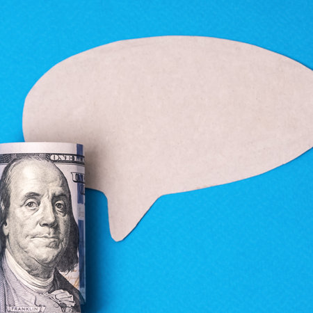 Rolled hundred dollar bank note with speech bubble, a copy space for text messsage. Money on blue background. High Quality photoの写真素材