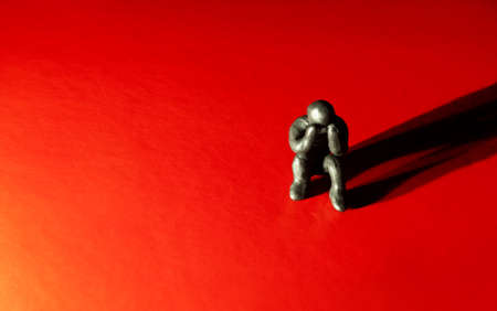 Depression, loneliness or other negative emotional concept - confused character made of clay sitting on red floor and highlighted with spotlightの写真素材