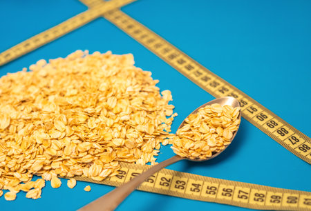 Diet food and Lose weight. Oat flakes scattered on blue and blurry background with measuring tape...