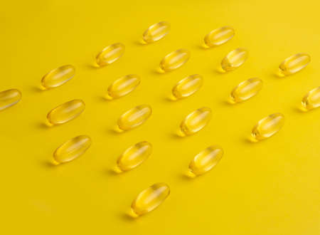 Fish oil omega 3 gel capsules on yellow background. Pills arranged in rows. High quality photoの写真素材