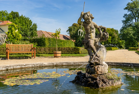 In the park, there is a beautiful fountain featuring a statue of a woman gracefully holding a trident. The serene setting includes lush greenery, blue skies, and a peaceful natural landscapeの写真素材
