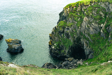 A grassy cliff overlooking the shimmering ocean on a sunny day, with fluffy clouds dancing in the blue skyの写真素材