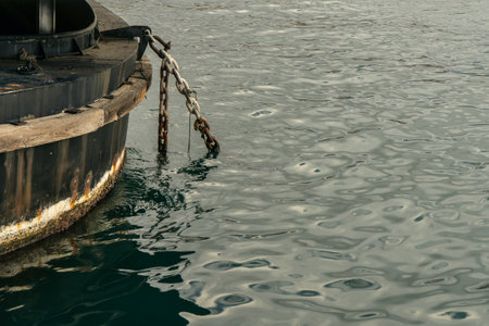 Rusty and weathered ship anchor chain on mooring bollard with sea surface on backgroundの写真素材