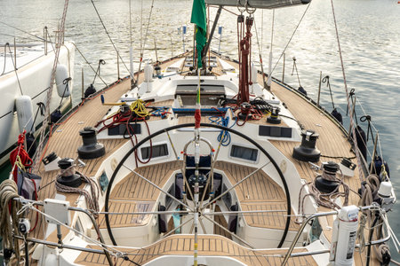 An image of a sailboats bow with a wooden deck and a steering wheel, set against a maritime...