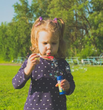 a 4 years old girl blowing soap bubbles in Park