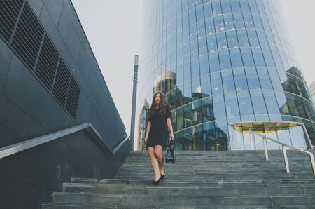 beautiful girl in a black dress walks down the stairs holding a bagの写真素材
