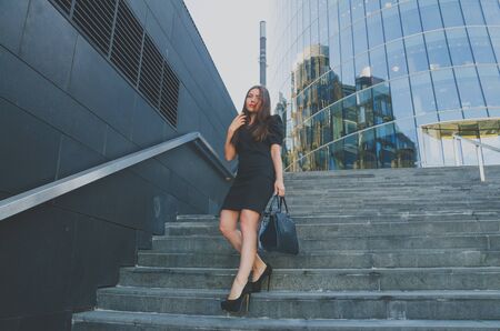 business girl in a dress walks down the stairs holding a bagの写真素材