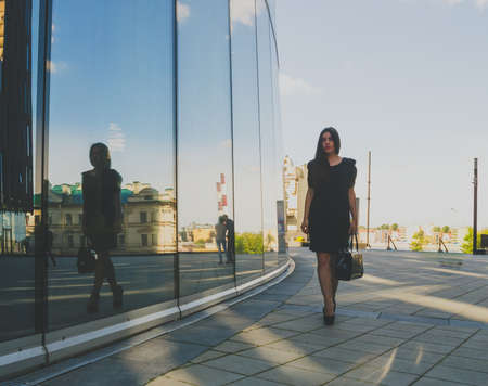 beautiful girl in a black dress goes in the background of the business centerの写真素材