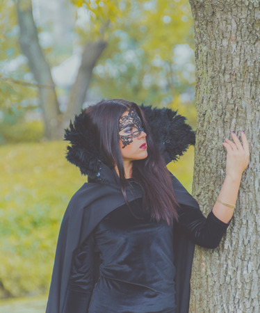 Park is beautiful girl in black robes standing near the tree.の写真素材