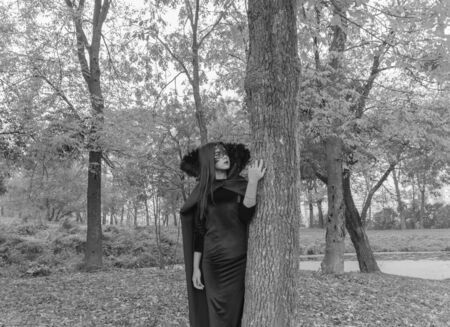 the image of Halloween pretty Girl in a dress and a mask put his hand on the tree Black and white.の素材 [FY31066673704]