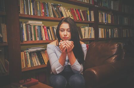 Beautiful girl sitting in the library with a mug of tea.のeditorial素材
