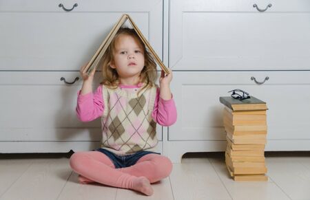 girl with glasses and a book on the head near the stack of old books.の写真素材