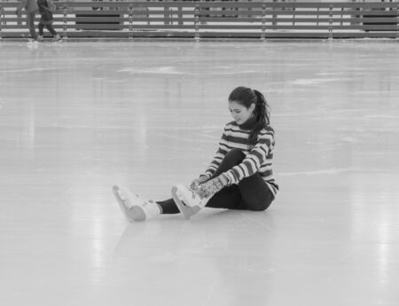 black white, pretty girl sitting on the ice tying skates.の写真素材