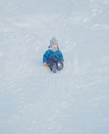 on a Sunny day on a snowy hill a child with a sled.の写真素材