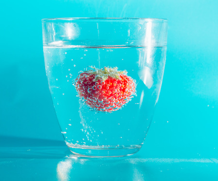 on a blue background strawberries in a glass with bubbles.の写真素材