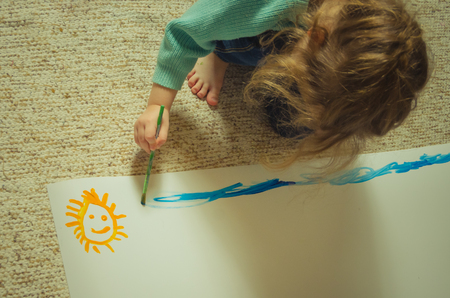 a child paints on paper, sitting on the floorの写真素材