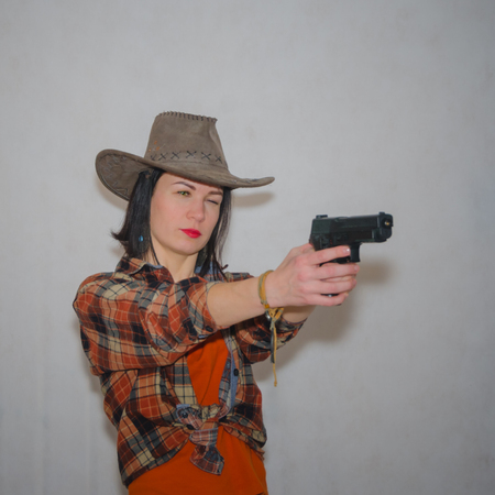 the girl the cowboy with a gun pointing on gray backgroundの写真素材