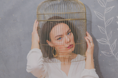 on the background of gray wall beautiful girl with a birdcage on his head, close-upの写真素材